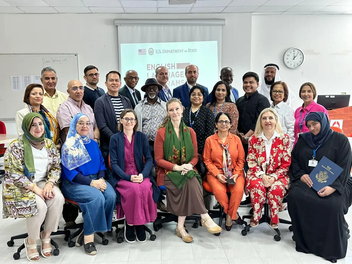 Faculty members at Bahrain Teachers College posing with US Embassy officials after a certificate ceremony in front of a U.S. Department of State English Language Programs screen